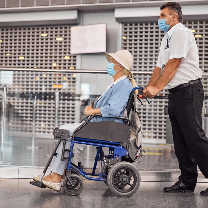 Side view of an airline male employee transporting an aged female passenger in a wheelchair