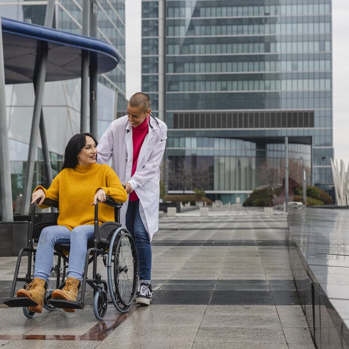 doctor pushes a young woman's wheelchair while giving her psychological support