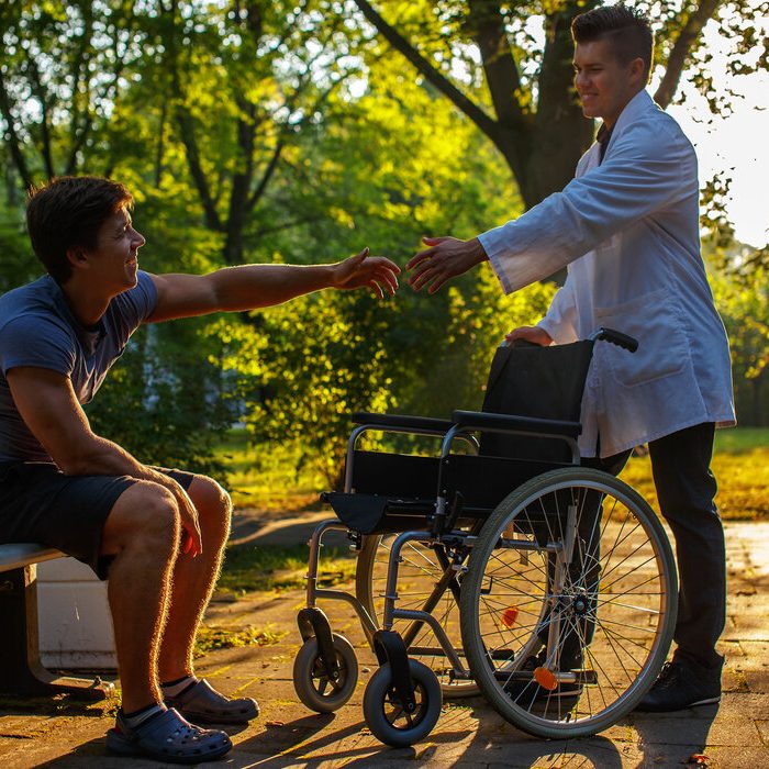 Young doctor helping one guy to stand up.